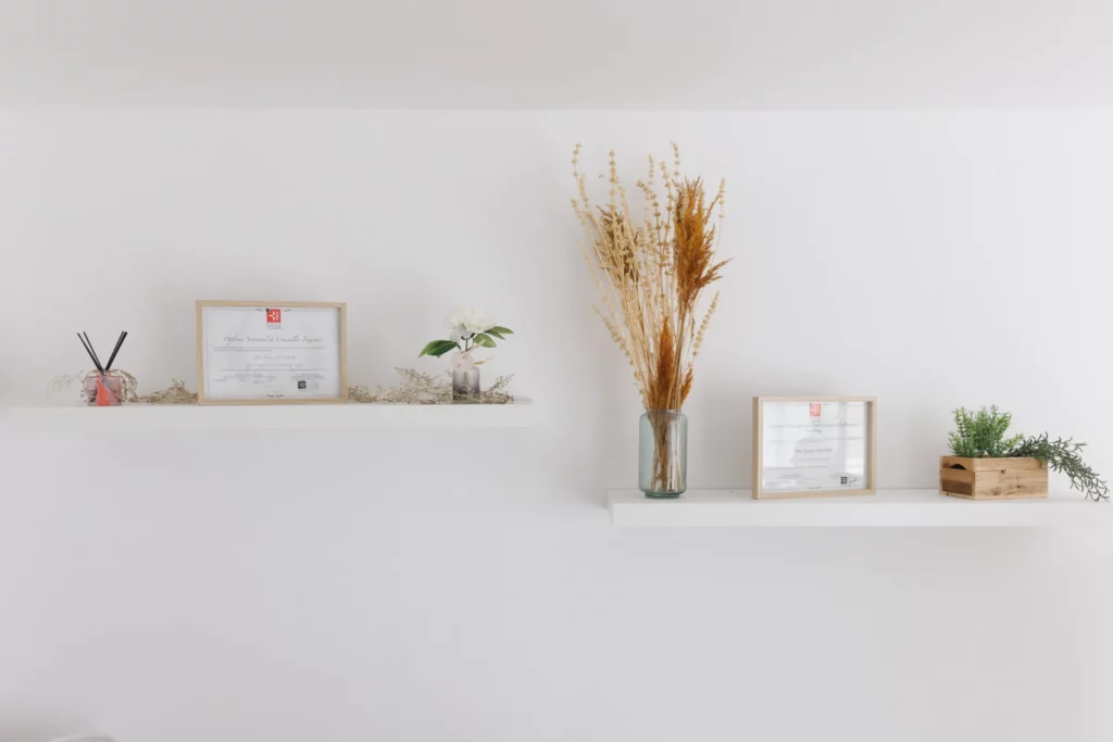 Décoration murale épurée avec étagères, fleurs séchées et diplômes encadrés.